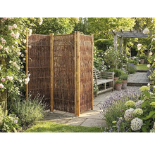 Trojdielna skladacia zástena z prútia v záhrade s kamennou dlažbou, kvetmi a drevenou lavičkou.