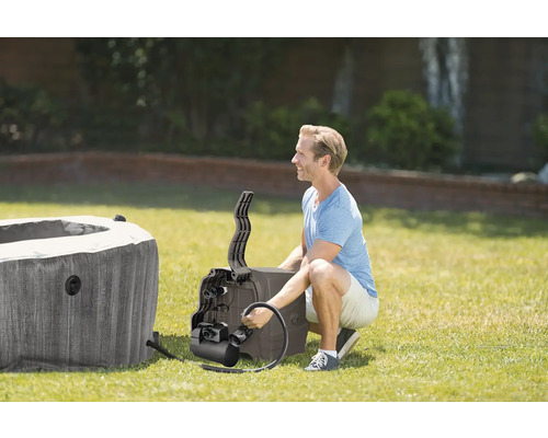 Muž inštaluje čerpadlo k nafukovacej vírivke v záhrade na trávniku.