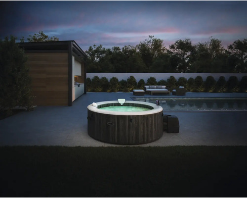 Nafukovacia vírivka Intex v tmavom drevenom dekore na modernej terase vedľa bazéna za súmraku s vonkajším nábytkom v pozadí.