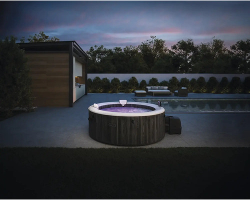 Nafukovacia vírivka Intex s kamenným dekorom na modernej terase s bazénom a záhradným nábytkom za súmraku.