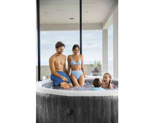 Rodina relaxuje v okrúhlej nafukovacej vírivke s tmavým dreveným dekorom na svetlej terase.