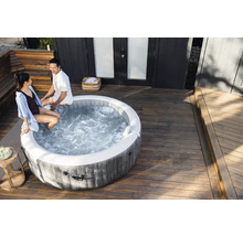 Okrúhla nafukovacia vírivka v dekore dreva na svetlej drevenej terase s dvomi osobami sediacimi na okraji.