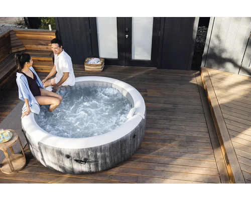 Okrúhla nafukovacia vírivka v dekore dreva na svetlej drevenej terase s dvomi osobami sediacimi na okraji.