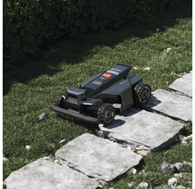 Robotická kosačka Segway Navimow prechádza cez kamenný chodník v záhrade.