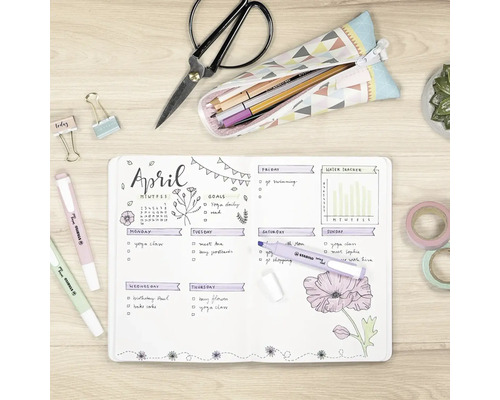 Pohľad zhora na svetlý, usporiadaný písací stôl s otvoreným bullet journalom, zvýrazňovačmi Stabilo Swing Cool, nožnicami a papiernictvom.
