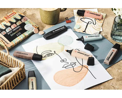 Jasná a usporiadaná scéna so zvýrazňovačmi Stabilo Boss Original NatureColors v prírodných tónoch na kresbe, s výtvarnými potrebami a kávou.