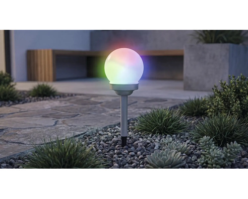 Solárne záhradné guľové svietidlo s viacfarebným RGB osvetlením, na zapichovacom hrote v štrkovom záhone s rastlinami.