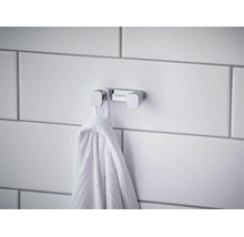 Dvojitý háčik na uteráky Hansgrohe z chrómu na dláždenej stene s poveseným uterákom.