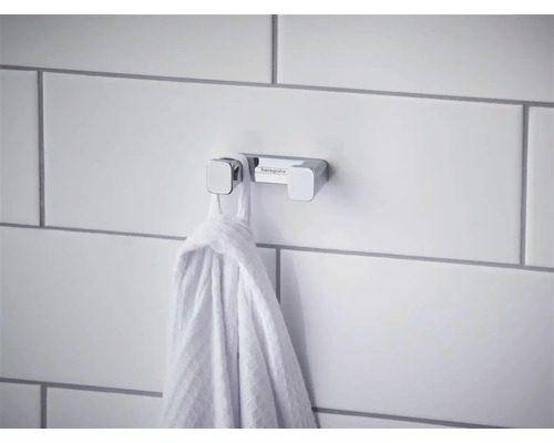 Dvojitý háčik na uteráky Hansgrohe z chrómu na dláždenej stene s poveseným uterákom.