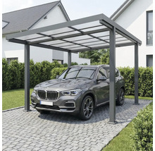 Moderný hliníkový prístrešok pre auto s priesvitnou strechou nad vozidlom na dláždenej príjazdovej ceste pri dome.