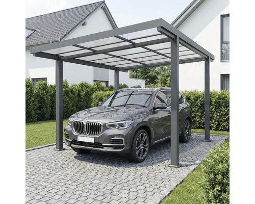 Moderný hliníkový prístrešok pre auto s priesvitnou strechou nad vozidlom na dláždenej príjazdovej ceste pri dome.
