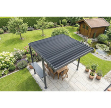 Voľne stojaca pergola s lamelovou strechou na svetlej terase v záhrade, vrátane dreveného nábytku, priľahlého jazierka a záhradného domčeka v pozadí.