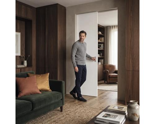 Muž otvára posuvné dvere v moderne zariadenej obývacej izbe s drevenými skriňami a pohovkou.