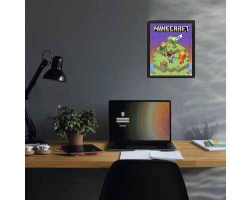 Plagát Minecraft v čiernom ráme na tmavej stene nad písacím stolom s notebookom a rastlinou.
