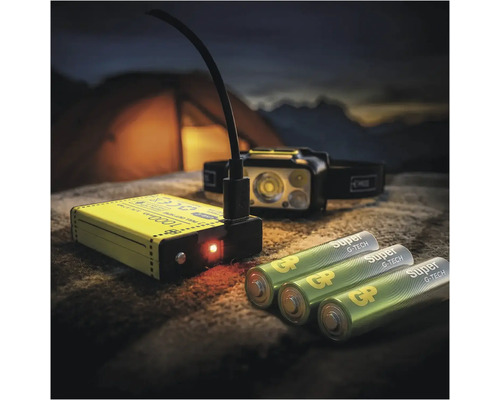 Čelovka s akumulátorom, káblom USB-C a tromi batériami GP Super G-Tech pri kempovaní pred stanom v horách.