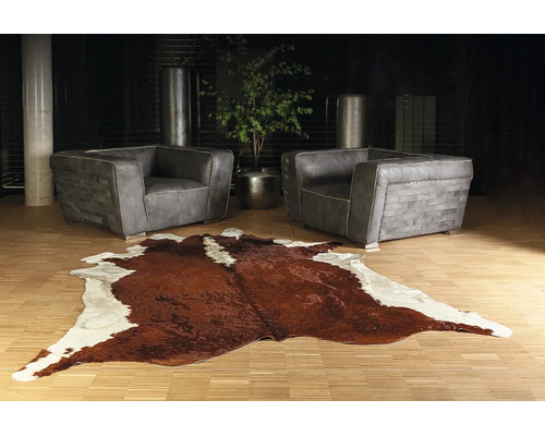 Moderná obývacia izba s dvoma sivými koženými kreslami a hnedo-bielym kobercom z hovädzej kože na svetlej drevenej podlahe.