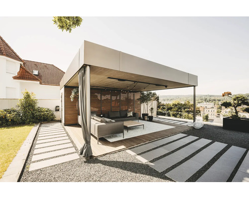 Moderná, svetlá kovová pergola s drevenou lamelovou stenou, závesmi a lounge nábytkom na drevenej terase v záhrade.