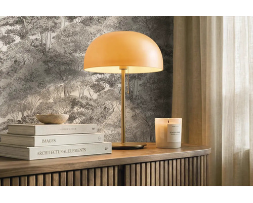 Moderná stolná lampa s okrúhlym tienidlom na drevenej komode pred lesnou tapetou, doplnená knihami a vonnou sviečkou. Svetlé a usporiadané.