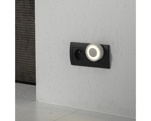 Okrúhle nočné LED svetlo s teplým svetelným krúžkom zapojené do dvojitej zásuvky na štruktúrovanej stene.