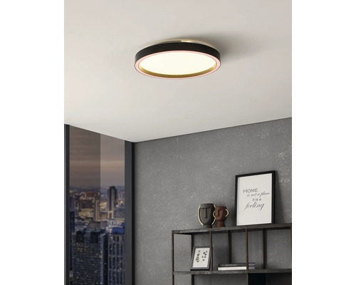 Okrúhle stropné LED svietidlo s čiernym krytom v moderne zariadenej izbe so sivou stenou a oknom s výhľadom na mesto.