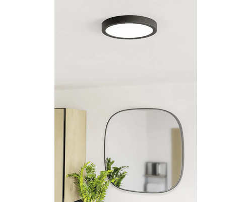 Moderné okrúhle stropné LED svietidlo v čiernej farbe vo svetlej miestnosti nad zrkadlom a rastlinou.