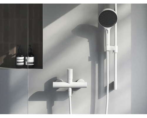 Moderný minimalistický sprchový set s ručnou sprchou na sprchovej tyči a sprchovou batériou vo svetlej, elegantnej kúpeľni.