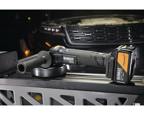 Akumulátorová uhlová brúska DeWalt Special Edition 18 V s akumulátorom a rukoväťou pred vozidlom.