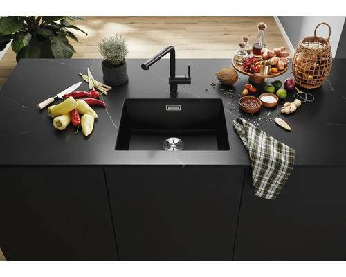 Moderný čierny kuchynský drez so zodpovedajúcou batériou na elegantnom kamennom kuchynskom ostrovčeku s ingredienciami a dekoráciami.
