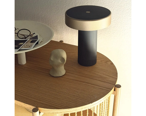 Moderná nabíjacia lampa na okrúhlom drevenom odkladacom stolíku s dekoratívnymi predmetmi.