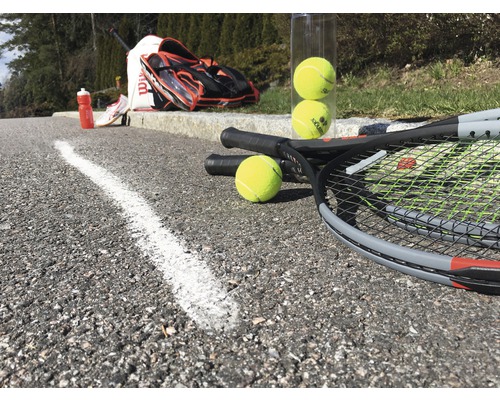 Tenisové rakety, tenisové loptičky, tenisová taška a fľaša na pitie na asfalte