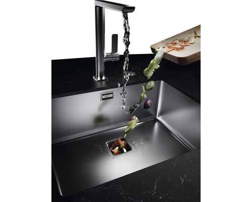 Kuchynský drez s drvičom odpadu, vodovodnou batériou a padajúcimi zvyškami zeleniny