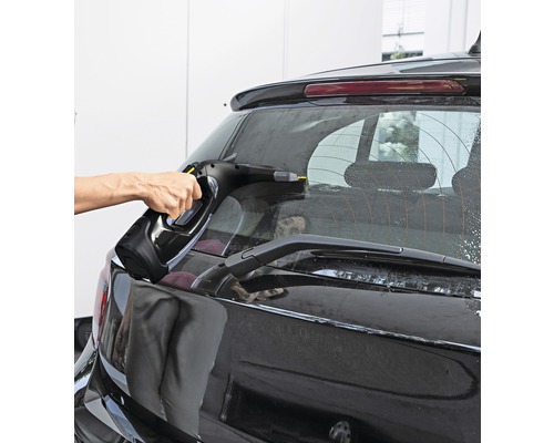 Osoba čistí zadné okno auta pomocou okenného vysávača.