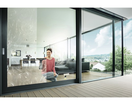 Žena umýva okná v modernej obývačke s presklenými posuvnými dverami a terasou.