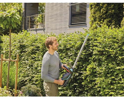 Muž strihá živý plot nožnicami na živý plot v záhrade.