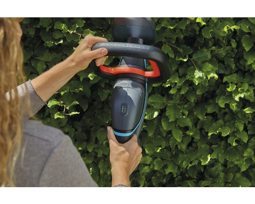 Osoba používa akumulátorové nožnice na živý plot Gardena pred živým plotom.