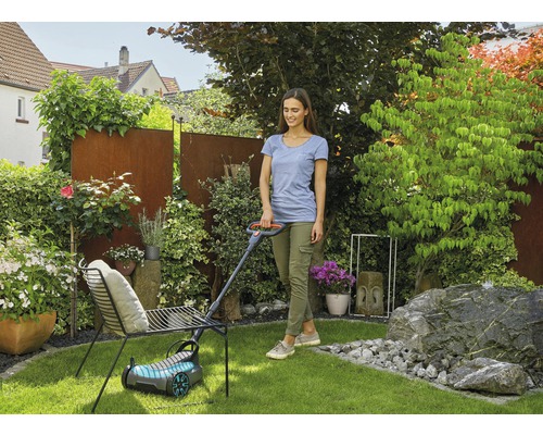 Žena kosí trávnik kosačkou na trávu v záhrade.