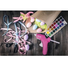 Zdobené veľkonočné vajíčka, tavná pištoľ, vodové farby, nožnice a stuhy na veľkonočnú dekoráciu na drevenom stole