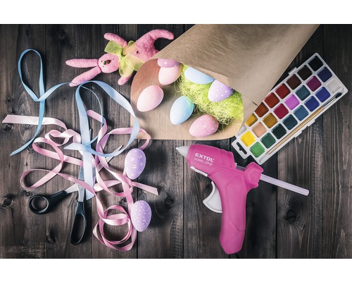 Zdobené veľkonočné vajíčka, tavná pištoľ, vodové farby, nožnice a stuhy na veľkonočnú dekoráciu na drevenom stole