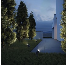 Exteriér moderného domu s trávnikom a stromami osvetlenými niekoľkými reflektormi.