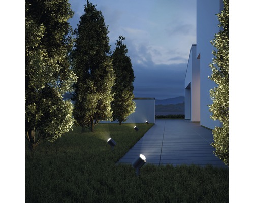 Exteriér moderného domu s trávnikom a stromami osvetlenými niekoľkými reflektormi.