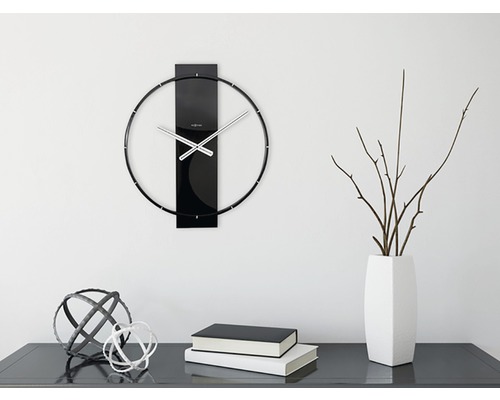 Nástenné hodiny s kovovými ručičkami a dekoráciou na komode