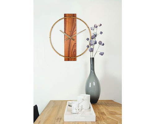 Nástenné hodiny s drevenými detailmi a zlatými akcentmi nad dreveným stolom s dekoráciami.