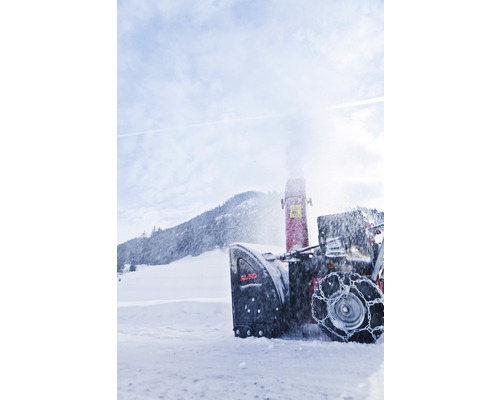 Snehová fréza v akcii pred zasneženou krajinou