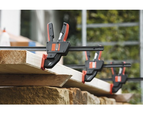 Niekoľko skrutkových zverákov upevňuje drevené dosky. Logo Bessey.