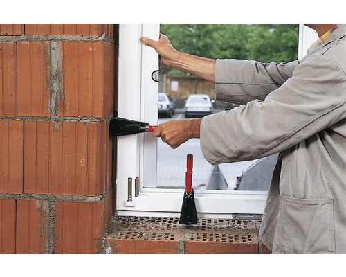 Remeselník montuje okno s okennými zdvihákmi do tehlovej steny.