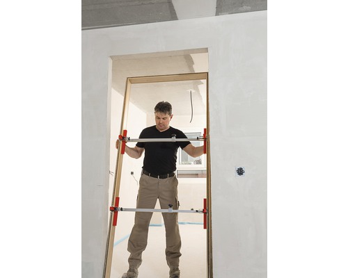 Muž montuje zárubňu dverí pomocou rozperky dverí v hrubej stavbe.