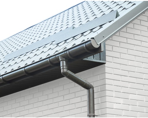 Strešný odkvap a zvod pri dome s škridlovou strechou a bielou tehlovou fasádou.