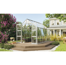 Skleník v záhrade s rastlinami a záhradným nábytkom na drevenej terase pred domom.