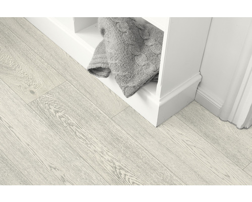 Svetlá drevená podlaha vedľa bielej police s pletenou dekou