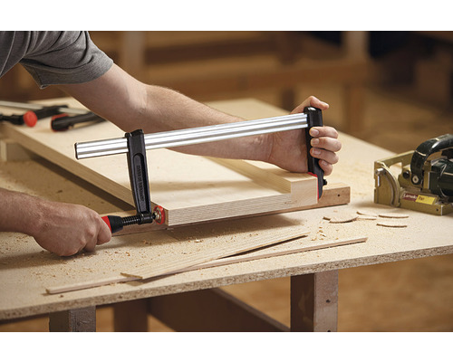 Osoba upevňuje drevo skrutkovou svorkou na pracovný stôl.